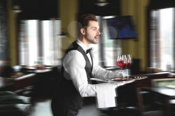Young hurrying waiter with glasses of wine in restaurant�