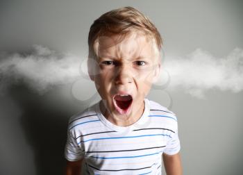 Portrait of angry little boy with steam coming out of ears on grey background�