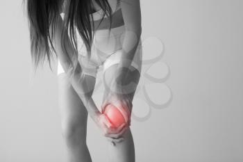Young woman suffering from pain in knee on light background�