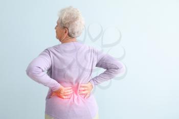 Senior woman suffering from pain in back against light background�