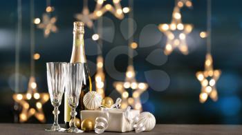 Champagne with gift and decor on table against blurred lights�