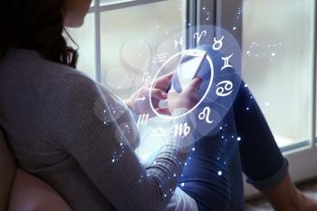 Young woman with mobile phone reading astrological forecast at home�