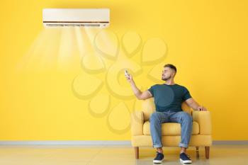Young man switching on air conditioner at home�