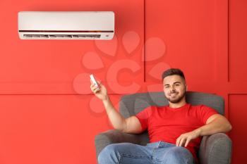 Young man switching on air conditioner at home�