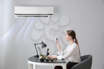 Young woman switching on air conditioner in office�