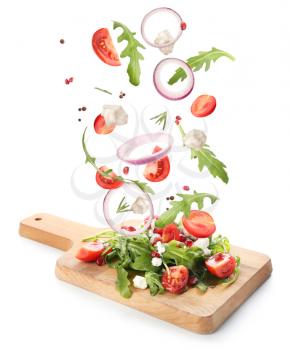 Board with tasty salad and falling ingredients on white background�
