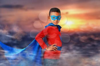 Cute African-American boy dressed as superhero outdoors at sunset�