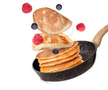 Tasty pancakes and berries falling on frying pan against white background�