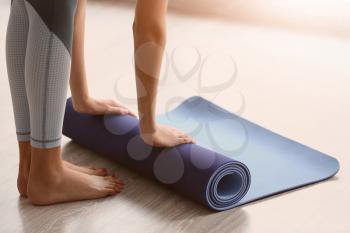 Beautiful young woman rolling yoga mat in gym�