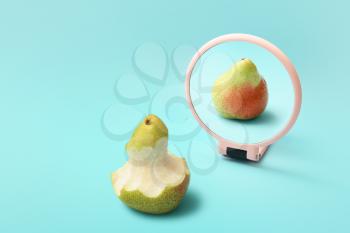 Bitten pear looking at its reflection in mirror on color background�