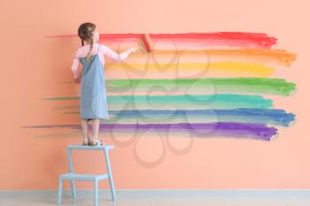 Cute little girl painting rainbow on wall�