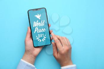 Female hands holding mobile phone with text WORLD PEACE DAY on screen against color background�