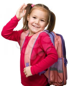 Portrait of a cute little schoolgirl with backpack, going to school and waiving bye-bye, isolated over white