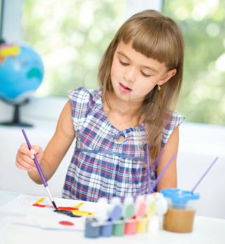 Little girl is painting with gouache while sitting at table