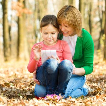 Mother and her daughter is playing with tablet, outdoor shoot