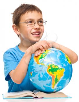 Little boy is holding globe while sitting at table, isolated over white