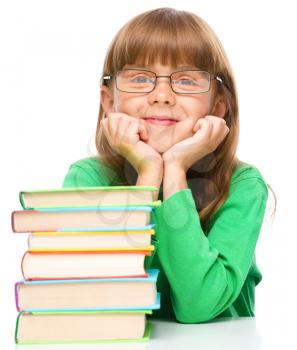 Cute little girl is reading a book while wearing glasses supporting his head with hands, isolated over white