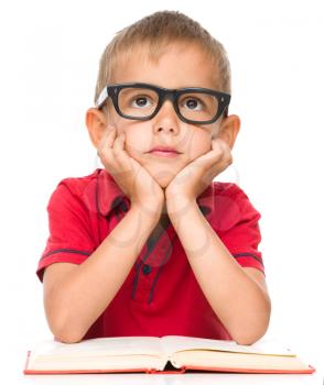 Cute little boy is reading a book while wearing glasses, isolated over white