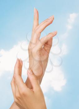 Two woman hands with moisturizer body cream against the sky
