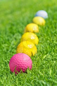 six golf balls on the green grass.Focus on the pink one.