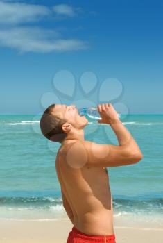 Young handsome man drinking water from bottle on the beach  