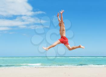 muscular young man jumping on the beach 