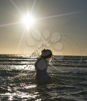 Beautiful woman is splashing the sea water with her hair against the sun