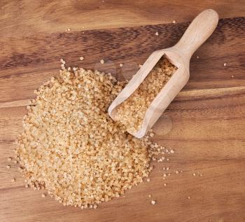 Brown sugar with wooden scoop over wooden background