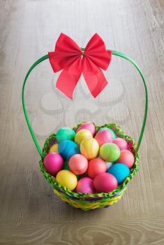 multicolored  Easter eggs in the wattled basket  on vintage wooden table 