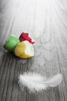 multicolored easter eggs and white feather on vintage wooden table 