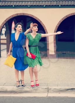 
Two beautiful girls in retro style  hailing  taxi in the street