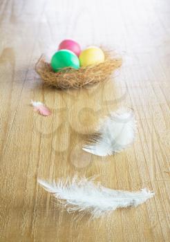 multicolored easter eggs and white feather on vintage wooden table 