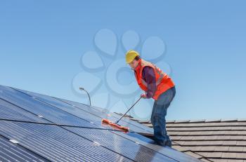 young worker cleaning solar panels on house roof
