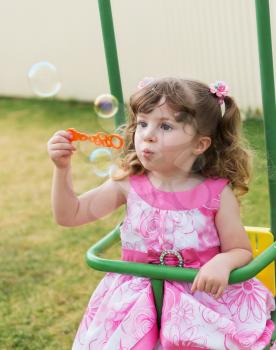 cute little girl swinging on seesaw and playing with soap bubbles