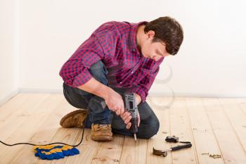 Young worker with screwdriver installing wooden flooring in the room