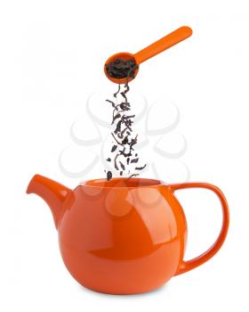 dry black tea falling from a spoon into  teapot isolated on white