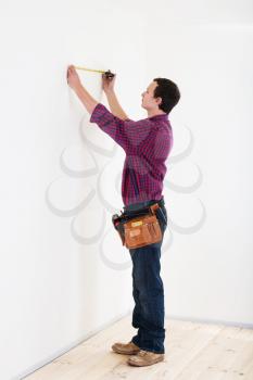 Young worker handyman with measuring tape near the wall in room
