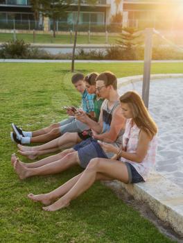 Group of young people with their digital devices outdoors at the evening light.
Concept of wireless communication and losing real one