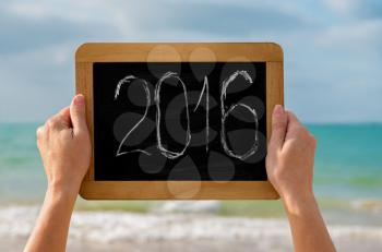 woman's hands with chalkboard and digits 2016 on it against the sea  - concept of new year, vacation and travel