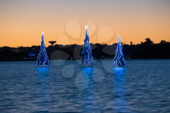 Christmas trees in the sea water with illumination at sunset