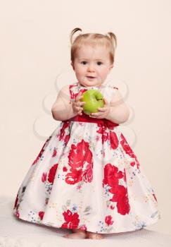 Beautiful baby girl with green apple on a light background. Retro toning