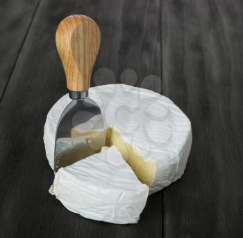 Fresh brie cheese and  cheese knife on rustic dark wooden table