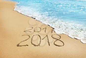 digits  2017 and  2018 on the sand seashore - concept of New Year and  Xmas and passing of time