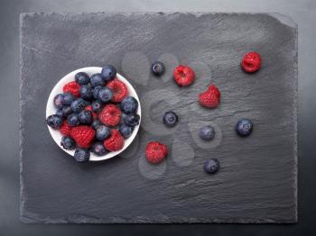 fresh raspberries  and bilberry berries scattered on black background.Top view