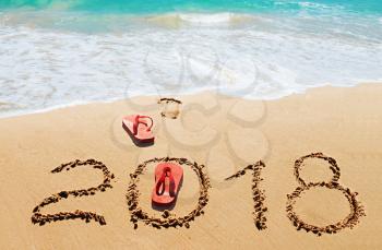 Red flip flops and digits 2018 on the beach sand.Concept of summer vacations, new year  and   Christmas