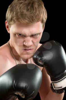 Furious young man in boxing gloves. Isolated on black