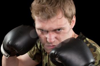 Portrait of angry young man in boxing gloves. Isolated on black