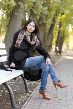 Perfect young woman sitting on a bench in autumn park