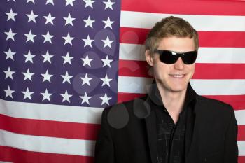 Smiling young man in sunglasses on a background of the American flag