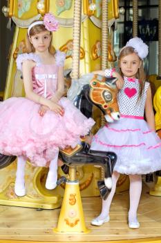 Two little elegant girls posing on the carousel